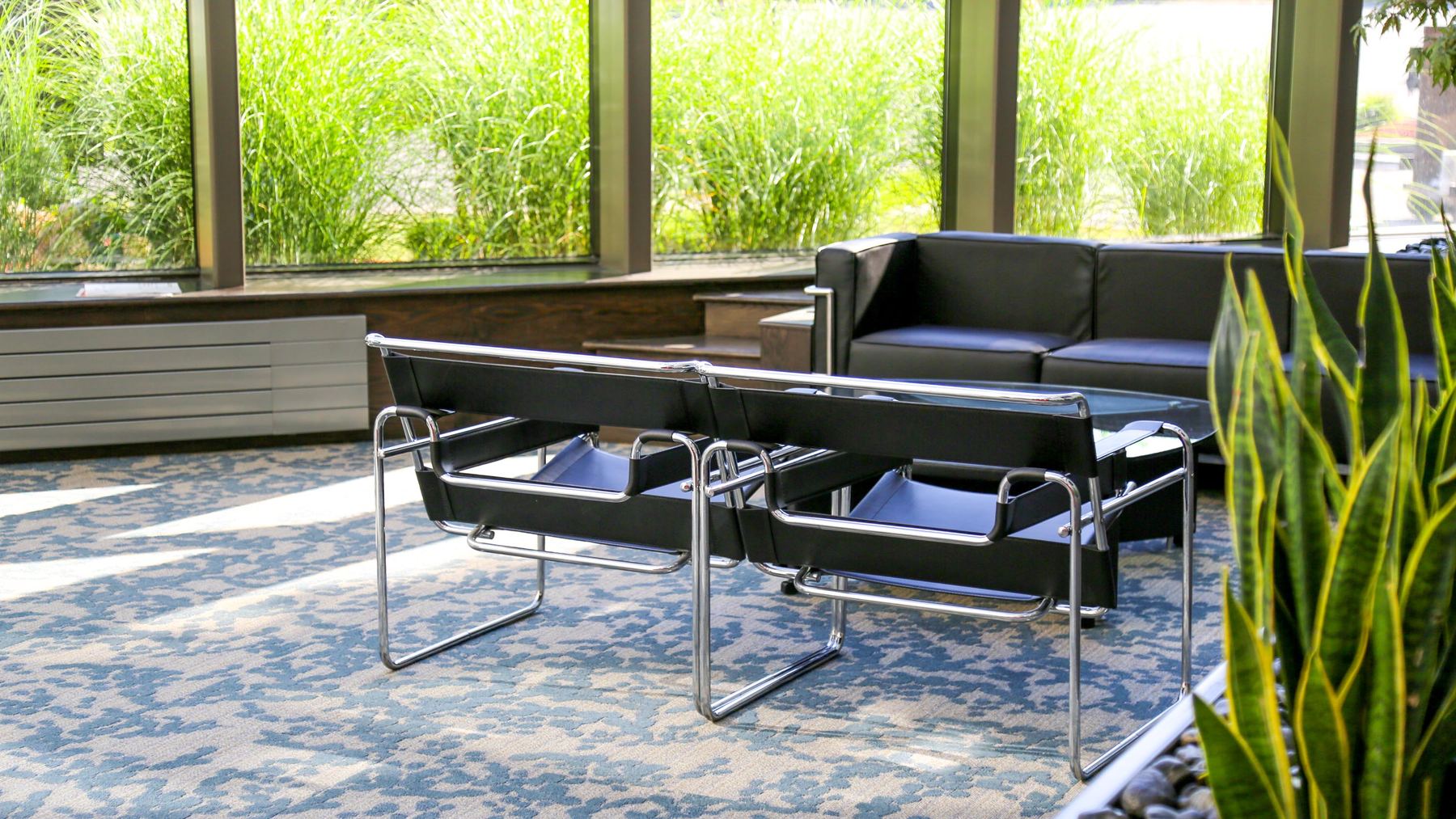 Sunlit lounge with leather chairs and a sofa beside floor-to-ceiling windows